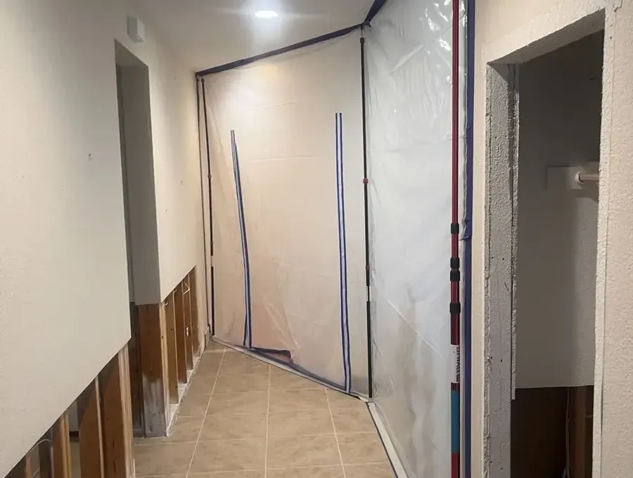 Containment plastic encloses a hallway with lower drywall removed during structural drying