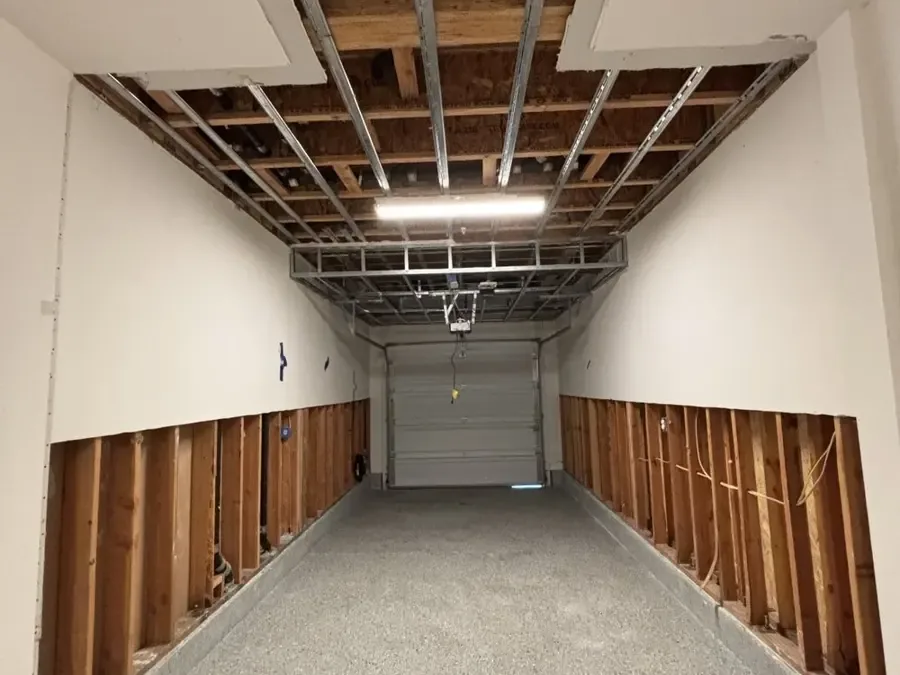 A garage has its ceiling and lower wall cavities exposed after water damage