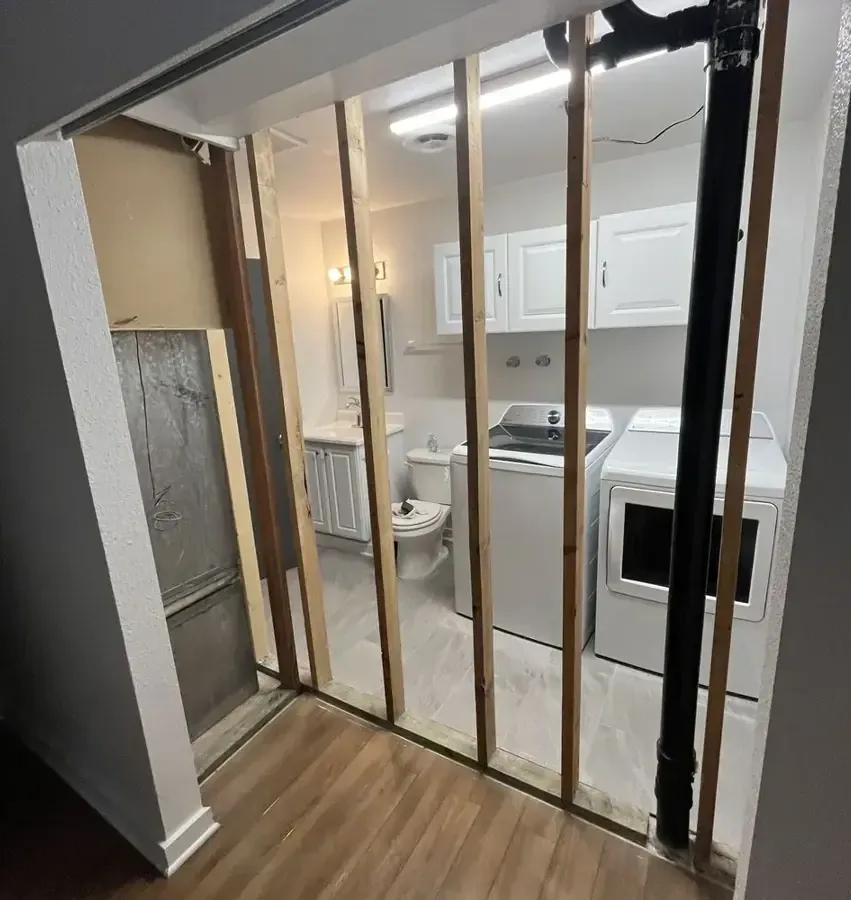An interior wall stands open to its studs beside a doorway