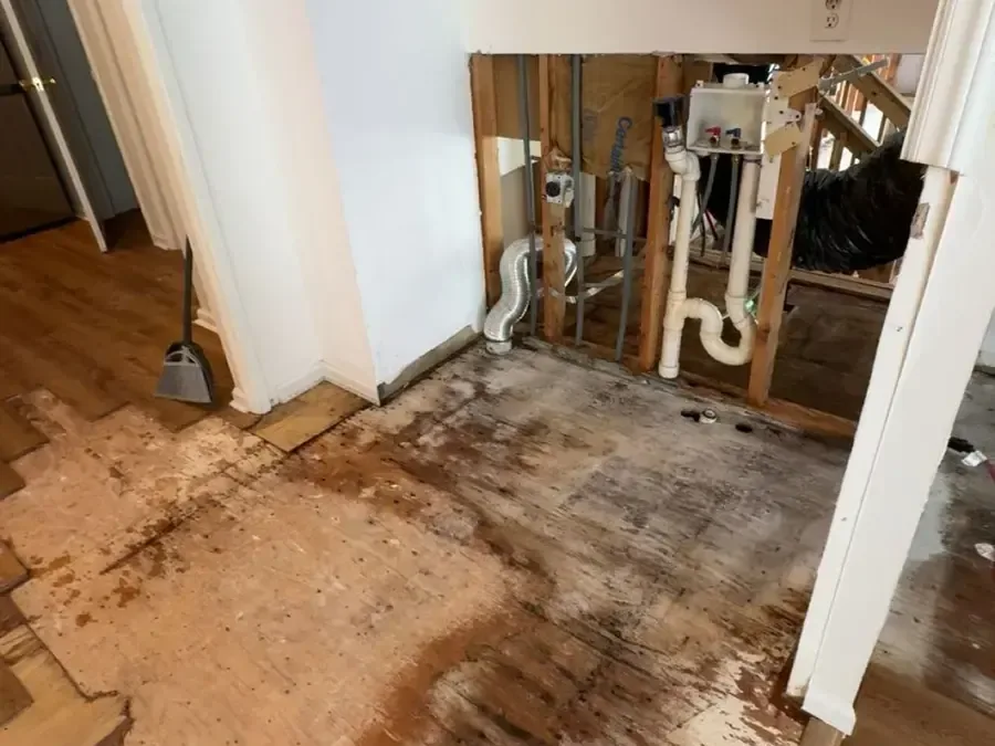 Opened wall framing exposes plumbing beside water-damaged flooring