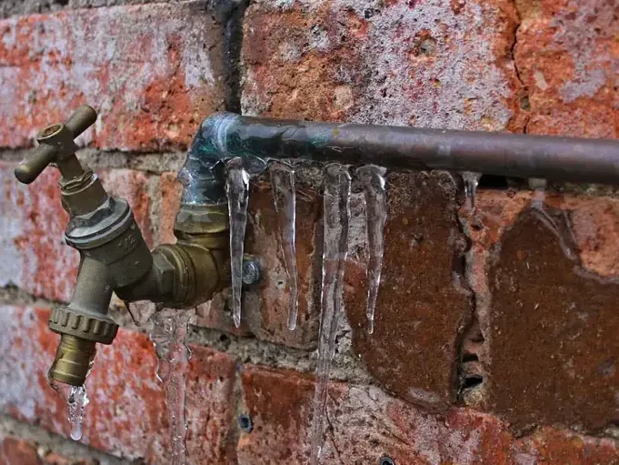 Icicles hang from an outdoor faucet and pipe against a brick wall