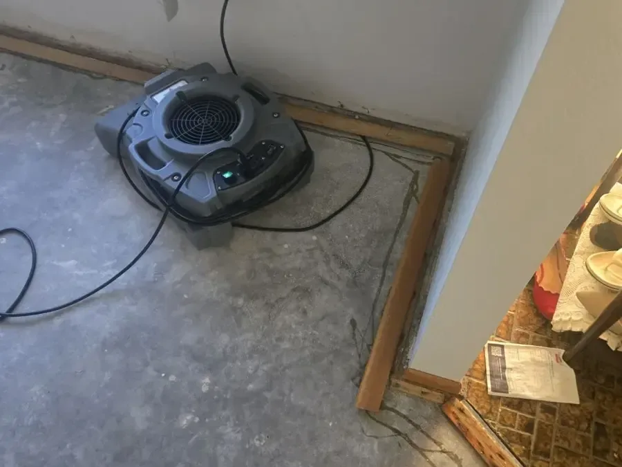 An air mover dries a bare concrete floor beside a doorway