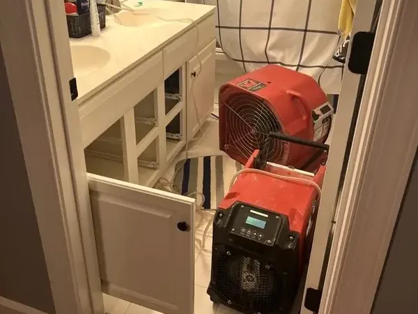 A red air mover and dehumidifier dry an opened bathroom vanity