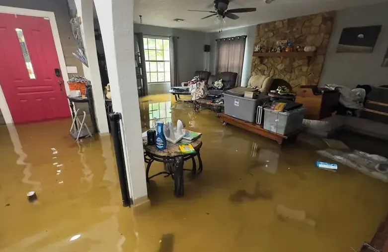Floodwater spreads across a room beside an open red door and furnishings