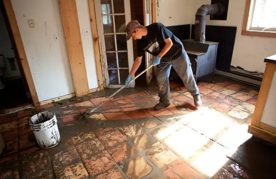 A worker scrapes muddy water and debris from a tile floor