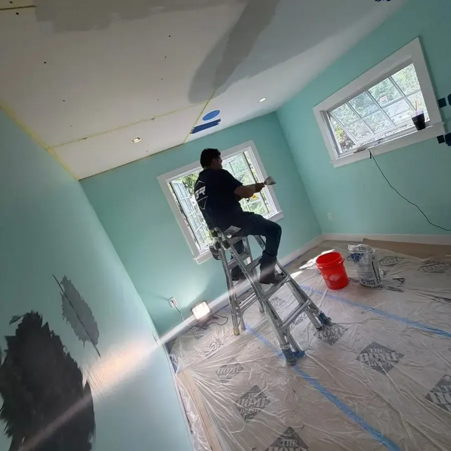 A worker stands on a ladder above protective plastic during interior drying work