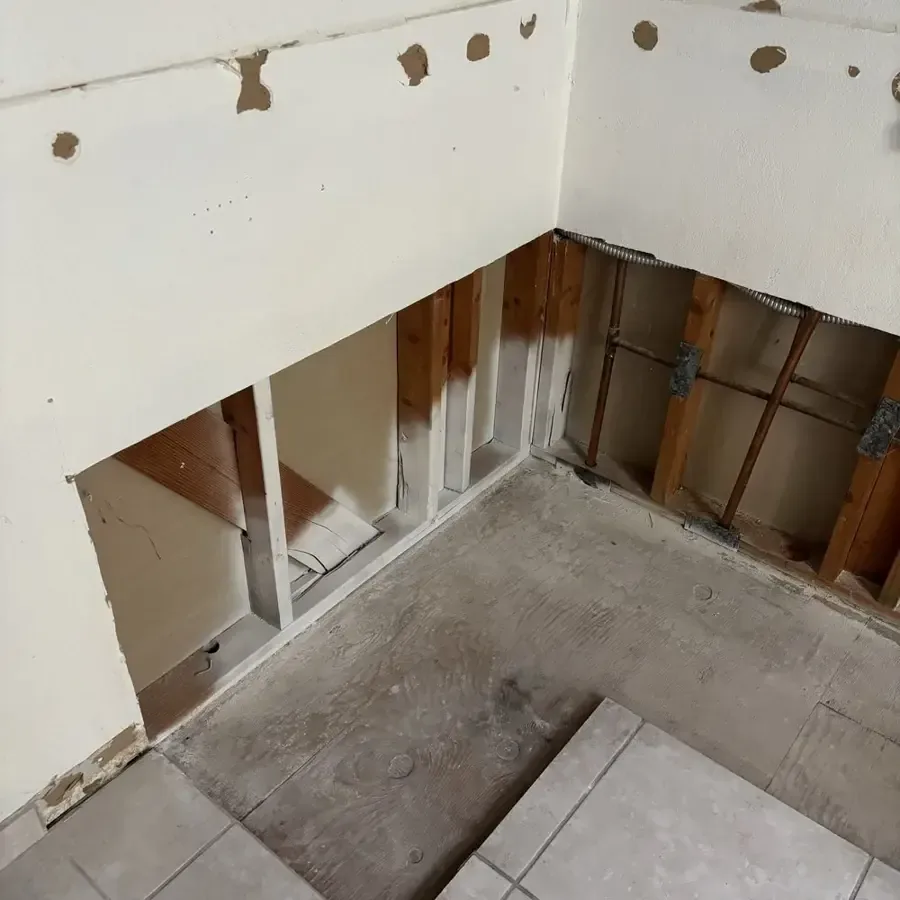 Opened wall framing above a tiled floor exposes the cavity for drying after leakage