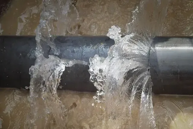 Water sprays from a split metal pipe above a wet surface