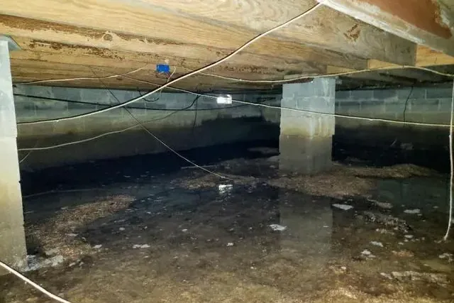 Standing water lies beneath exposed joists in a raised-floor crawl space