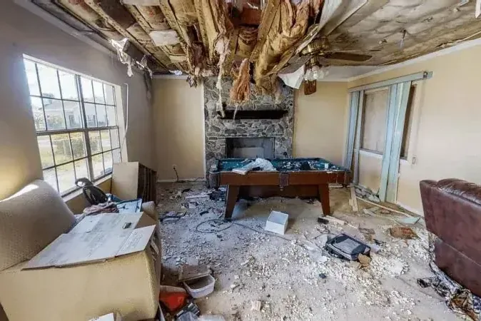 Wet insulation hangs from an opened ceiling above a damaged room