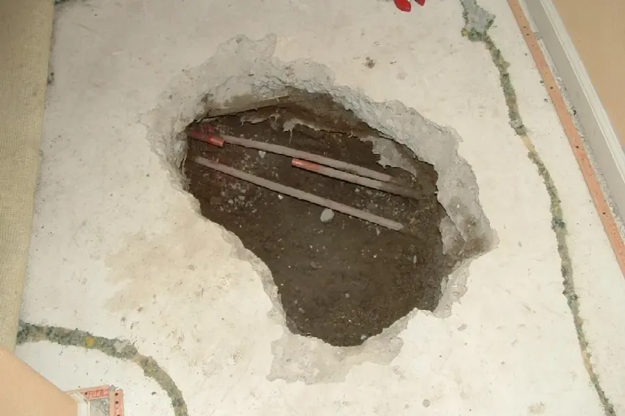 An opening in a concrete floor exposes buried copper water pipes