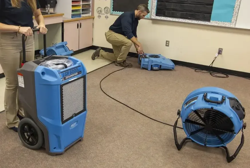 Air movers and a dehumidifier stand on carpet during a room dry-out